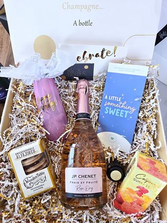 Birthday celebration gift box: sparkling rosé bottle, pink 'Happy Birthday' champagne flute, 'a little something sweet' chocolate bar, snickerdoodle cookies and gummy candies nestled in gold-and-white shredded paper.