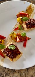 Bite-sized gourmet dessert: puff pastry squares topped with toasted coconut, caramelized banana, fresh strawberry slices and basil, plated with a caramel smear on a white plate.
