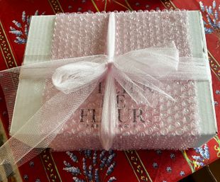 Gift box wrapped in pink bubble wrap and tied with a sheer pale-pink organza bow, sitting on a red lavender-patterned tablecloth