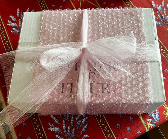 Gift box wrapped in pink bubble wrap and tied with a sheer pale-pink organza bow, sitting on a red lavender-patterned tablecloth