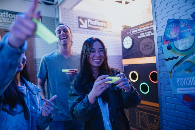 Young friends playing a neon-lit arcade game indoors — smiling woman holding a glowing controller while colorful circular targets light up on the game cabinet.