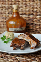 Close-up of juicy barbecue ribs glazed in sauce on a white plate with a scoop of creamy potato salad and parsley, rustic wicker placemat and amber sauce bottle blurred behind