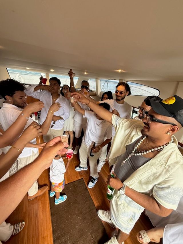 Lively yacht party: group of friends in white outfits raising shot glasses onboard with ocean views, summer celebration vibe.