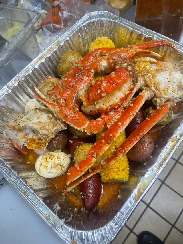 Cajun-style seafood boil in an aluminum tray with bright orange crab legs, corn on the cob, red and yellow potatoes, smoked sausage and boiled eggs tossed in garlic-butter and seasoning