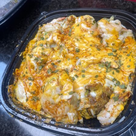 Spicy cheesy shrimp takeout in a black container — plump shrimp smothered in melted cheddar and creamy white sauce, dusted with paprika and chopped chives