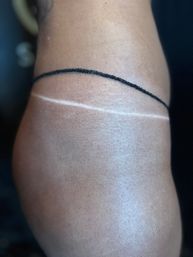 Close-up of an upper thigh showing a light tan line across the skin and a thin black anklet-style string.