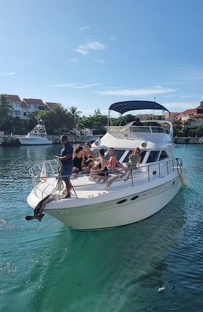 Group relaxing on the bow of a white luxury yacht in turquoise tropical marina waters with palm trees and blue sky, vacation vibe.