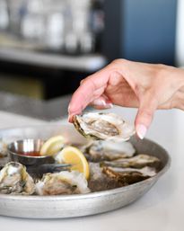 Hand picking a fresh raw oyster from a chilled platter of oysters on ice with lemon wedges and cocktail sauce at a seafood restaurant