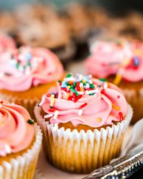 Close-up of a golden cupcake with swirled pink frosting, multicolored rainbow sprinkles and a white paper liner on a serving tray