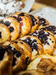 Glossy blueberry Danish pastries with cream cheese filling displayed on a bakery tray
