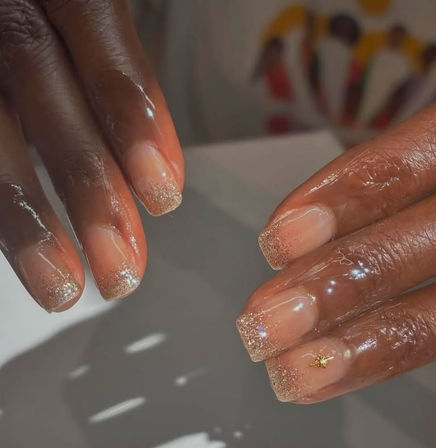 Close-up of glossy short square nails with a nude base and gold glitter French tips, featuring a tiny gold star accent — chic manicure nail art.