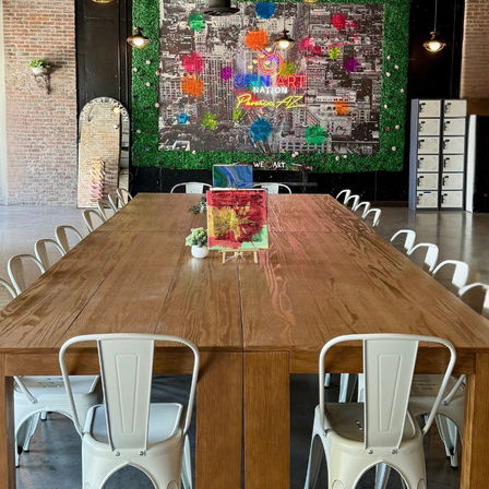Bright Phoenix, AZ art studio with a long wooden communal table, white metal chairs, colorful spin-art mural and mini easels