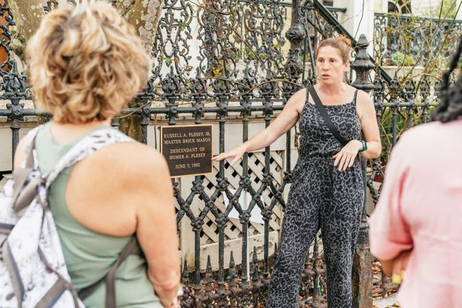 Tour guide pointing to a historic plaque on ornate wrought-iron fence during a small-group walking tour in a historic neighborhood.