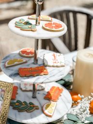 Three-tier marble dessert stand with colorful citrus-slice, leaf-shaped, and a 'Happy Birthday' iced sugar cookie on an outdoor party table