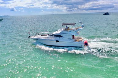 Sunlit white motor yacht cruising through turquoise coastal waters under a partly cloudy blue sky, leaving a foamy wake — vibrant boating seascape.