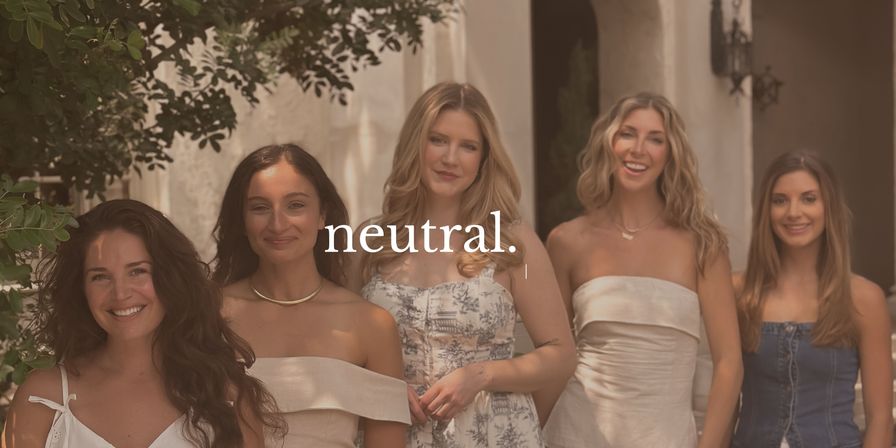 Five smiling women in neutral-toned summer dresses posing in a sunlit Mediterranean-style courtyard with leafy trees and stucco archways, with the word "neutral." overlaid