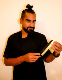 Smirking chef portrait with man bun and beard, wearing a black chef coat and holding a large Japanese-style kitchen knife.