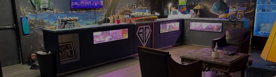 Cozy neon-lit indoor lounge with a long glass display counter beneath a colorful mural, plush armchairs around a carved wooden coffee table, ambient lamps and modern decor