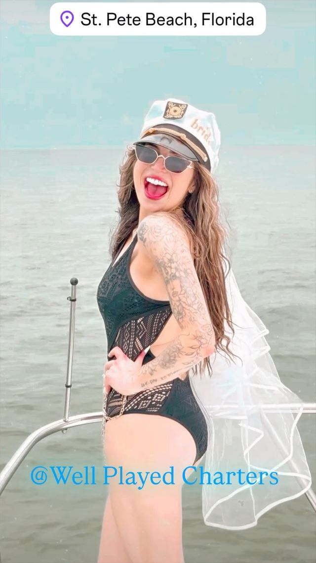 Smiling woman in a captain’s “bride” hat and veil, wearing sunglasses and a black lace swimsuit, posing on a boat with the calm ocean at St. Pete Beach, Florida