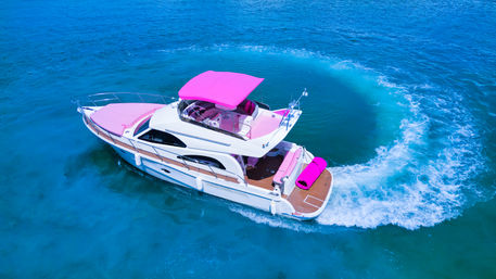 Aerial drone shot of a white luxury motor yacht with bright pink canopy and cushions making a circular wake in clear turquoise sea