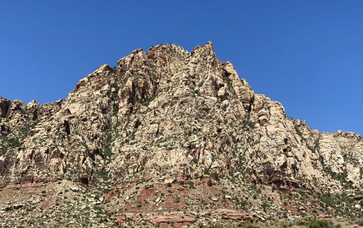 Towering red-and-white sandstone cliffs rising from desert scrub under a clear blue sky