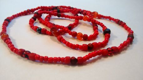 Close-up of coiled vibrant red beaded strands and necklaces with mixed glass and wooden beads on a white background
