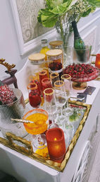 Festive holiday bar setup on a mirrored gold tray with champagne in ice, cranberry cocktails with sugared rims, extra glassware, citrus garnish, red votive candle and green vase foliage.