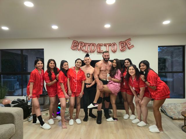 Indoor bachelorette party group photo: women in matching red pajamas and one in pink pose with two male entertainers under a rose-gold "BRIDE TO BE" banner.
