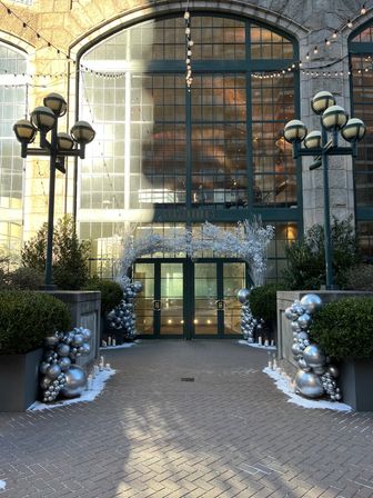 Downtown historic stone building entrance with large arched windows and green double doors, framed by silver balloon garlands, snowy branches, string lights and candles