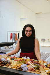 Smiling woman arranging a large colorful charcuterie grazing board with cheeses, cured meats, grapes, berries and crackers in a bright modern studio event space