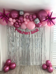 Indoor party photo backdrop with pink and fuchsia balloon garland, metallic starburst balloons, mirrored disco cubes, silver fringe curtain and floor balloon clusters