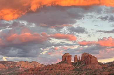 Glowing pink-orange sunset clouds over Sedona, Arizona red‑rock buttes and mesas in a dramatic desert landscape