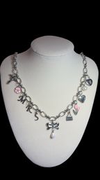 Silver charm necklace on a white display bust featuring MRS letter charms, bow pendant with teardrop pearl, pink enamel flower and tulip charms, heart lock, purse and pearl accents — boutique-ready bridal gift jewelry.