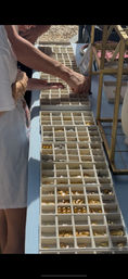 Close-up of hands browsing small gold and silver jewelry and charms organized in divided trays on a blue vendor table at an outdoor market