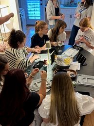 Group of friends at a home kitchen table enjoying a jewelry-making beading party and craft night with bead trays, tools, wine and snacks.