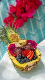 Vibrant tropical pineapple bowl filled with acai scoops, dragon fruit slices, strawberries, blueberries, blackberries and granola on a turquoise patterned background