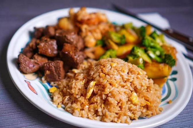 Close-up of a hearty Asian-style dinner plate: golden egg fried rice, seared beef cubes and broccoli stir-fry on a patterned ceramic plate.