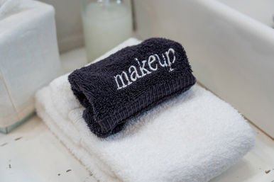 Dark gray towel embroidered with "makeup" folded on a white bath towel on a bathroom countertop