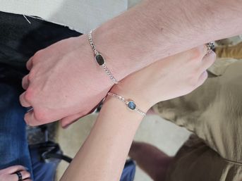 Close-up of two overlapping wrists wearing matching silver chain bracelets with dark faceted stones — minimalist matching bracelet set