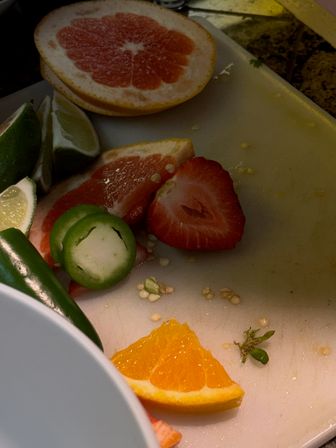 Sliced grapefruit, lime wedges, orange slice, strawberry and jalapeño rings on a white cutting board — colorful citrus and pepper prep in a home kitchen