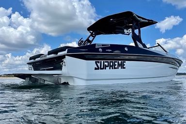 Sleek white-and-black speedboat with bold 'SUPREME' decal gliding through coastal blue water under a bright, partly cloudy sky.