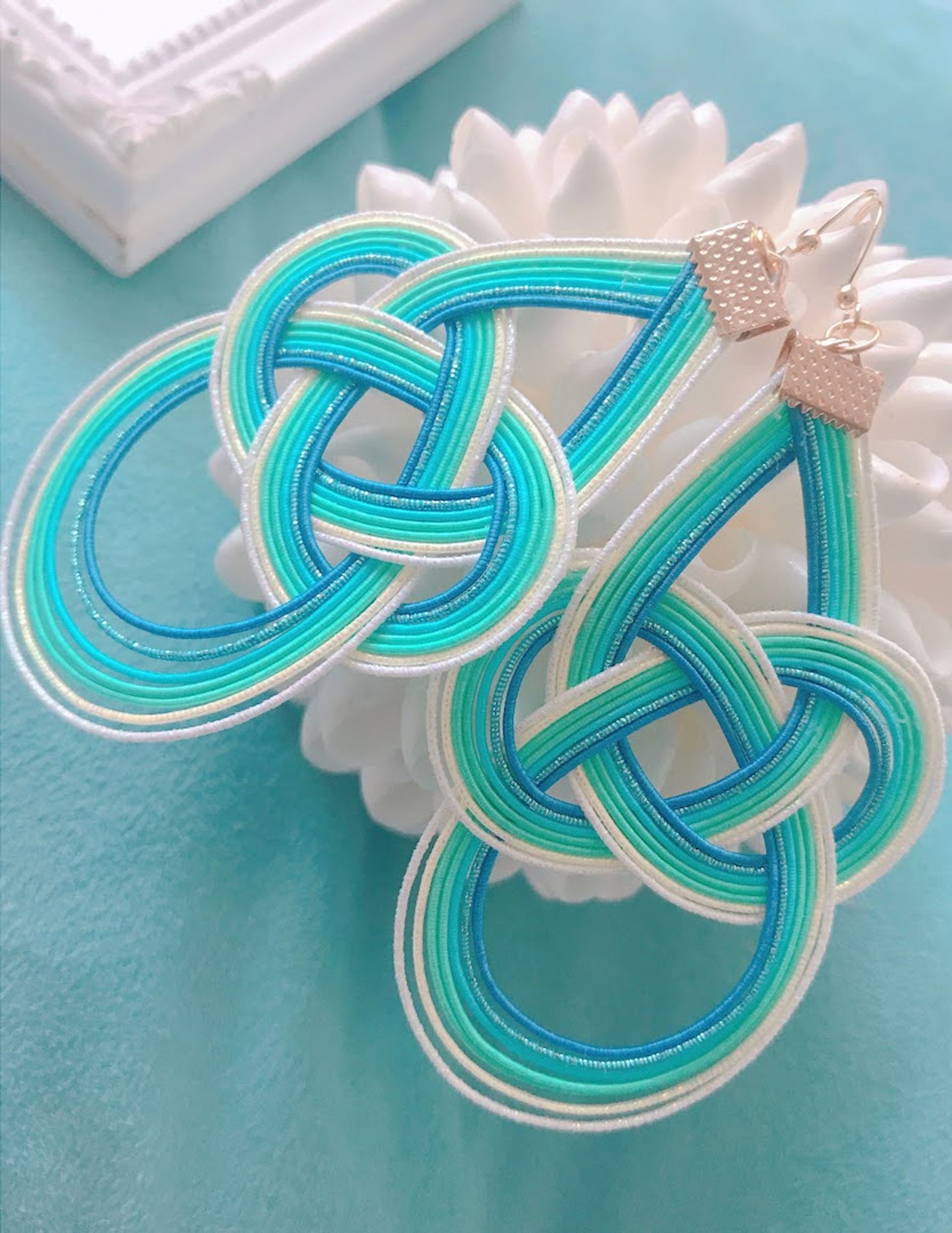 Ocean-inspired turquoise, teal and white knotted cord earrings with gold hooks – intricate looped mizuhiki-style design on an aqua background
