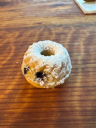 Close-up of a single mini blueberry donut dusted with powdered sugar on a rustic wooden table