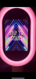 Event selfie station touchscreen framed by pink LED ring light displaying 'TAP TO START' over neon geometric lines