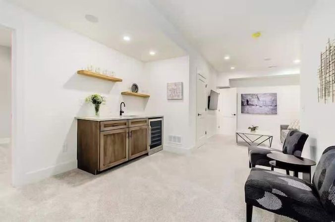 Bright finished basement home with wooden wet bar, built-in wine fridge, floating shelves, modern wall art, wall-mounted TV and cozy seating area