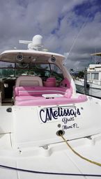 White motor yacht docked at a marina with bright pink cushioned seating, radar dome, onboard speakers and a cloudy sky overhead.