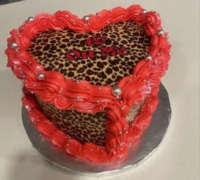 Heart-shaped leopard-print cake with bright red ruffled buttercream border, silver dragee accents and red lettering reading "is on me" — bold party dessert