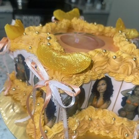 Close-up of a yellow-gold celebration cake with swirled buttercream rosettes, gold dragees, glossy candied orange slices, pink and white ribbon bows, and edible photo panels of women.
