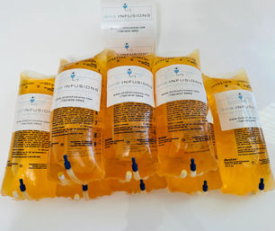 Bright orange IV vitamin drip bags with labels and tubing lined up on a white countertop, ready for wellness infusion therapy.