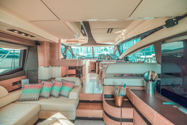 Luxurious yacht salon with cream leather lounges, colorful zigzag pillows, wood cabinetry, a champagne bucket on a side table and marina city skyline visible through wraparound windows.